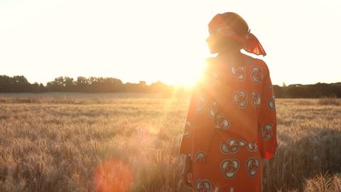 African woman farmer in traditional clothes standing in a field of crops, wheat or barley, in Africa at sunset or sunrise
