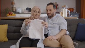 The Muslim pregnant woman shows her husband the cardigan she knits for their babies who will be born. Baby cardigan display concept. - Powered by Shutterstock - Get 15% off with code: PIKWIZARD15