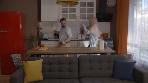 Hearing the Muslim woman with a turban singing in the kitchen with a beater, her husband came running and danced together. Entertainment concept in the kitchen. Slow motion video