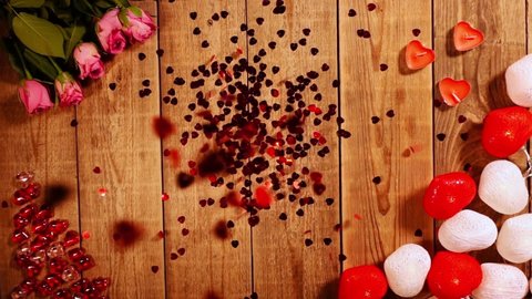 Red sparkles heart are falling from above in slow motion on wooden surface decorated Valentine day. Roses and candles romantic background. Concept of making surprise for soulmate. Spending lovely date