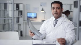 Medium portrait shot footage of mature Middle Eastern pulmonologist holding X-ray picture speaking on camera during online meeting