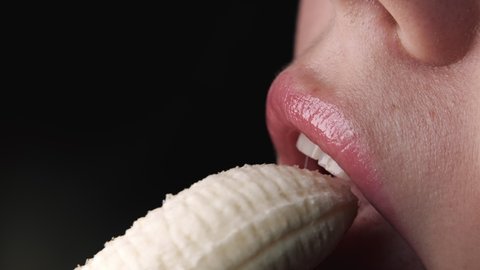 Sexy young woman seductively bites and eating fresh banana. Close-up view of female mouth, sensual footage. Slow motion.