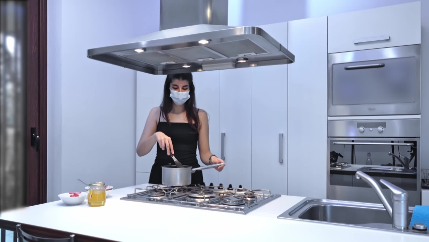 Young woman cooking food for delivery in protective mask.