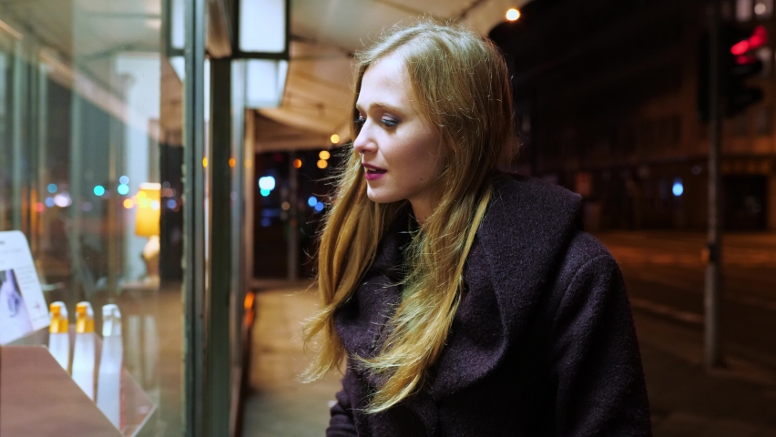 [4k] young blonde woman likes what she sees in the shop-window in the evening