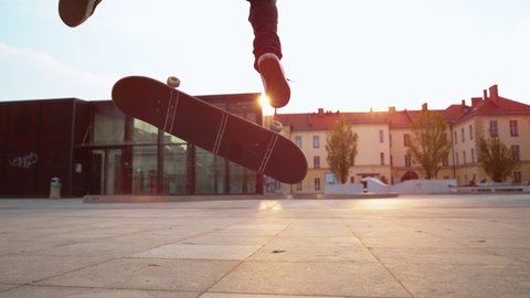 SLOW MOTION TIME WARP, CLOSE UP, LOW ANGLE, LENS FLARE, DOF: Unrecognizable skater does a flip trick while riding around a square. Cinematic shot of a skateboarder doing a nollie kickflip at sunset.