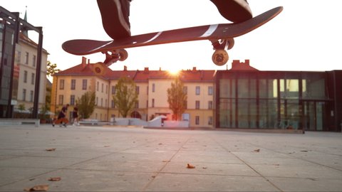 SLOW MOTION TIME WARP, CLOSE UP, LOW ANGLE, LENS FLARE, DOF: Cinematic shot of a skateboarder doing a nollie kickflip at sunset. Unrecognizable skater does a flip trick while riding around a square.