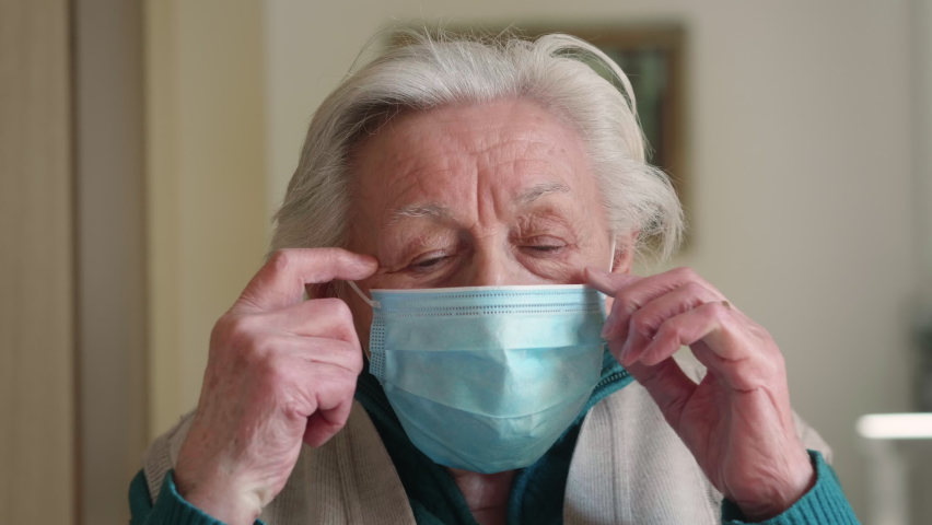 Authentic cinematic close up shot of retired disabled grey hair senior woman is taking off protective medical mask and smiling in camera at home. Concept of covid-19, healthcare, care for older people Royalty-Free Stock Footage #1067271451