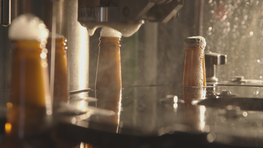Close-up of bottles getting filled with beer on a modern industrial machine. Foam getting out of bottles and overflowing. Factory, brewery concept. | Shutterstock HD Video #1067276002