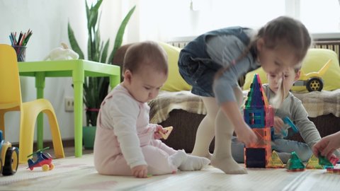 Childhood, family, motherhood, parenthood concept - young happy mother spends time playing magnets blocks builds castle with toddler kids. Joy Children have fun together in playroom floor on