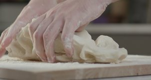 Making dough in the kitchen. The process of kneading homemade dough for pasta or cakes where hands knead it. Cinematic background 4K slow motion video.