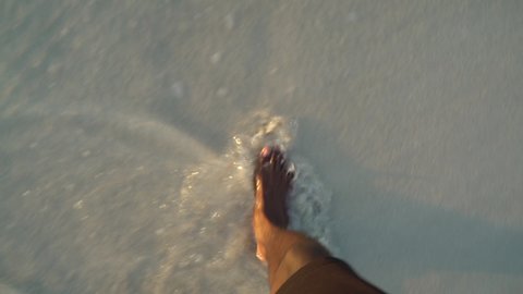 Close up view of an adult black male walking on a beautiful beach during sunset. African American male feet walking on the beach.  