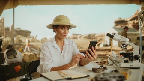 Archaeological Digging Site: Famous Female Archaeologist Doing Research, Uses Smartphone to Post Discovery of Fossil Remains, Ancient Civilization Culture Artifacts on Internet Social Media