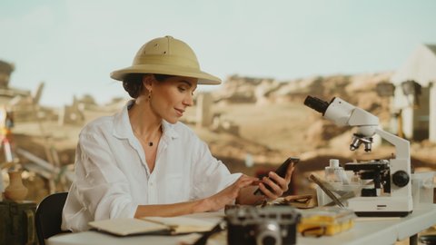 Archaeological Digging Site: Great Female Archaeologist Doing Research, Uses Smartphone to Scan and Analyse Fossil Remains, Ancient Civilization Culture Artifacts. Historians work on Excavation Site