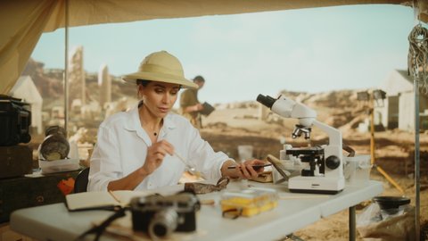 Archaeological Digging Site: Great Female Archaeologist Doing Research, Uses Smartphone to Share Discovery of Fossil Remains, Ancient Civilization Cultural Artifacts on Internet Social Media