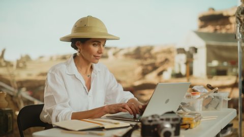 Archeological Digging Site: Great Female Archaeologist Doing Research, Using Laptop, Analysing Fossil Remains, Ancient Civilization Culture Artifacts. Team of Historians work on Excavation Site