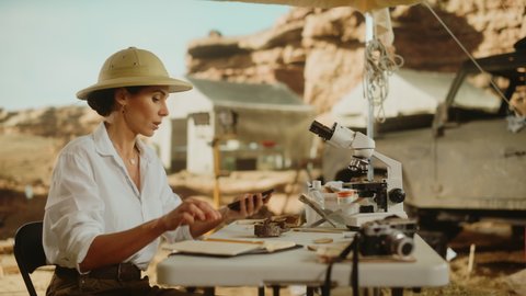 Archeological Digging Site: Great Female Archaeologist Doing Research, Uses Smartphone to Scan and Analyse Fossil Remains, Ancient Civilization Culture Artifacts. Historians work on Excavation Site