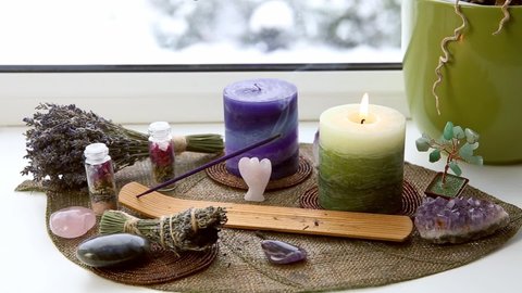 Small good feng shui altar in home on window sill on leaf shape table mat, snowy Nordic nature on background. Incense candle smoking, gemstones for decoration.