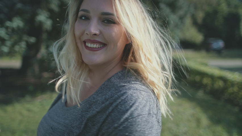 Closeup sensual smile of blond woman plus size. Nature landscape. Body positive people. Happiness model girl at sun leaves trees. Laughing lady in grey dress. Hapy lifestyle. Portrait cinematic shot