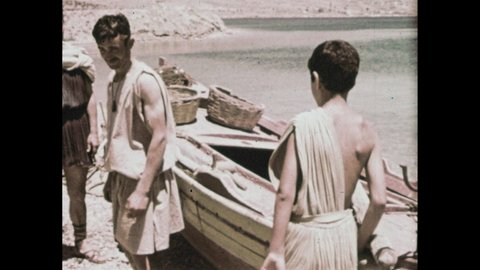 1960s: People paddle small sailboats. Men in togas stand by boat. Ancient greek map. Men point to map.