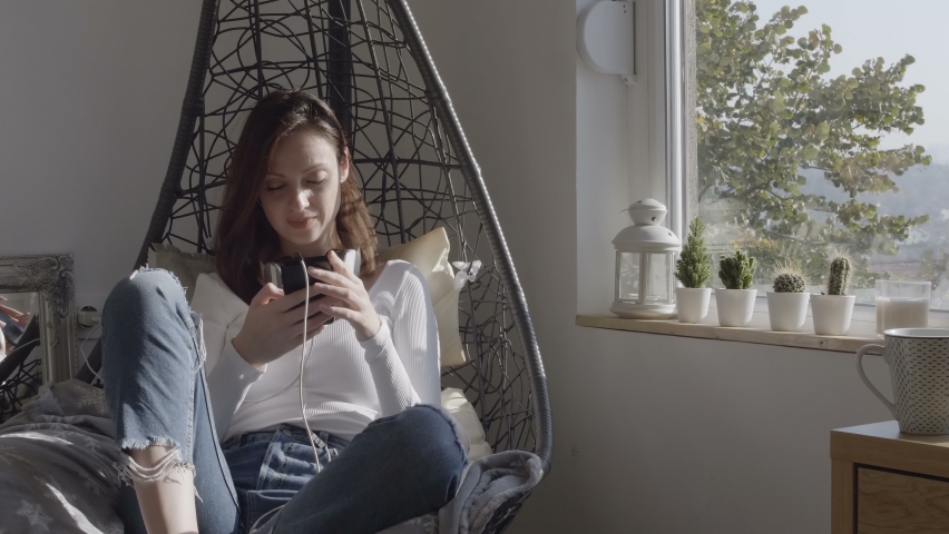 Young woman sitting in hanging chair near window at home