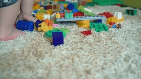 Close-up video shot. White carpet with pile, children's designer. The child's foot is visible. With his right hand, the child takes the red construction element and puts it on the carpet.