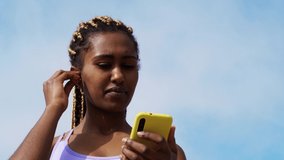 African fitness woman listening music playlist on smartphone outdoors with sky on background - Fit training during coronavirus outbreak 