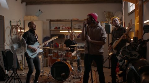 WIDE Friends playing music during their rock band rehearsal repetition inside a garage. Vocals, guitars and drums. Shot with 2x anamorphic lens