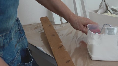 Left-handed woman painting white on wood using a sponge roller. Close up.