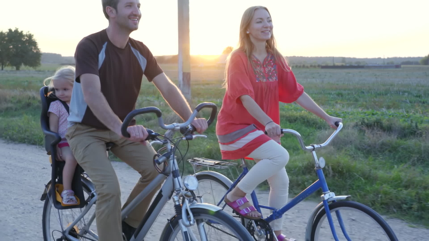 Young couple on a bike with their little daughter at sunset.