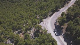 Aerial view over mountain road going through forest at National Park. Clip. Summer landscape with a bending road and green trees in a hilly region. 