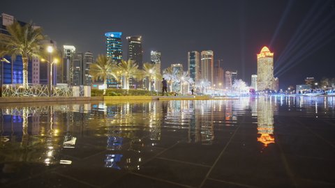Doha ,Qatar- December 11 2020:West bay skyscrapers  night shot taken from Sheraton park  with fountain  in the foreground,  palm trees , people and cars moving in the Corniche 