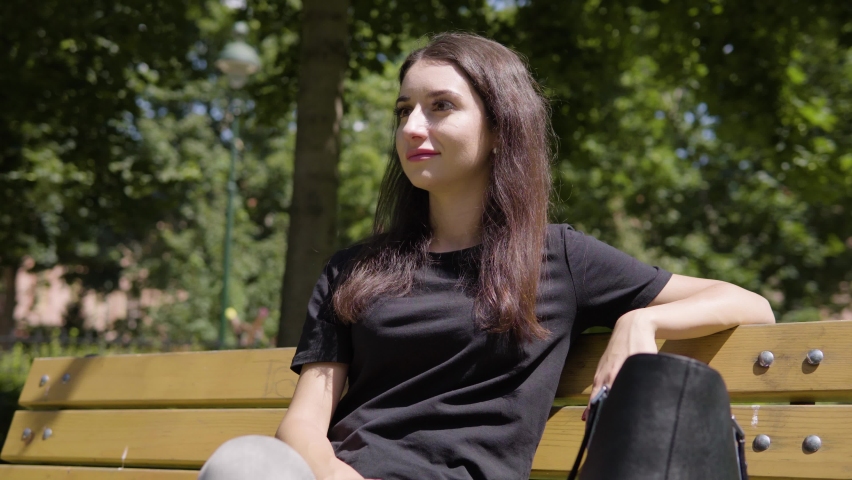 A young Turkish woman sits on a bench and enjoys the sun with a smile in a park in an urban area on a sunny day Royalty-Free Stock Footage #1067324695