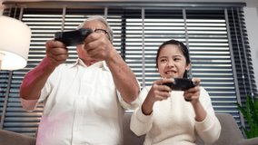 Happy family girl and uncle having fun relaxing together, playing video games on bed at home. Funny daughter and old man expressing emotions while enjoying their hobby spend their free time together.