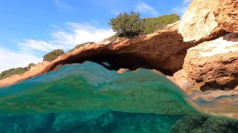 Underwater split video from rocky sea cave formation in calm emerald sea beach of Avlaki, Porto Rafti, Mesogeia, Attica, Greece