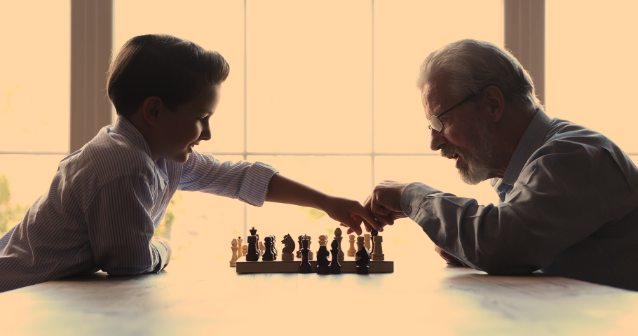 Smart happy little child boy playing chess game with caring old senior retired grandfather indoors, focused multigenerational family enjoying developing intellectual skills and strategic vision. Royalty-Free Stock Footage #1067336149