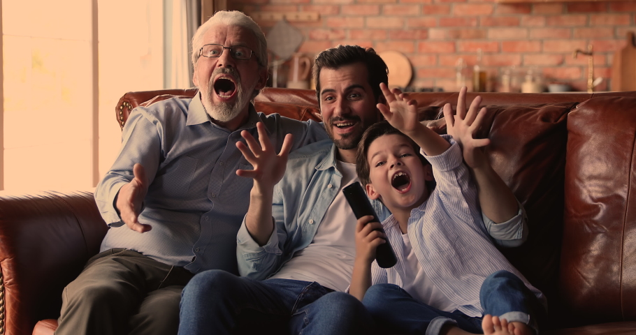 Overjoyed emotional middle aged old retired man watching sport TV match with happy grownup son and little kid grandson, celebrating favorite team win, enjoying spending weekend time together. | Shutterstock HD Video #1067336254
