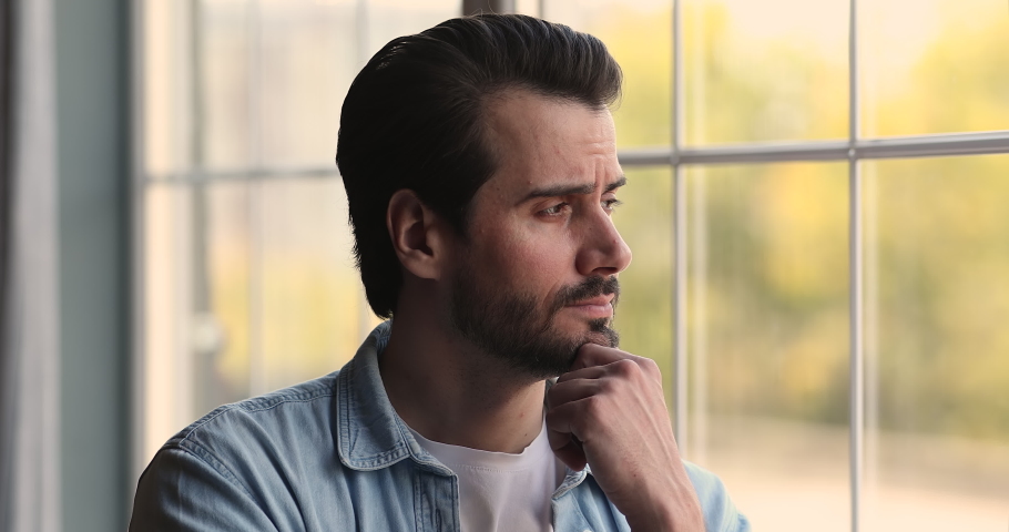 Head shot frustrated millennial man looking out of window, thinking or personal problems solution, regretting mistakes, suffering from depression or divorce break up relations, feeling lonely at home. | Shutterstock HD Video #1067336830