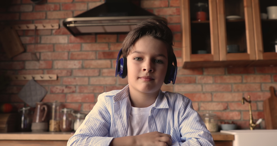 Adorable small 7s kid boy wearing wireless headphones, looking at camera, enjoying online class, holding video call meeting seminar training with teacher, distant education e-learning concept. Royalty-Free Stock Footage #1067337250
