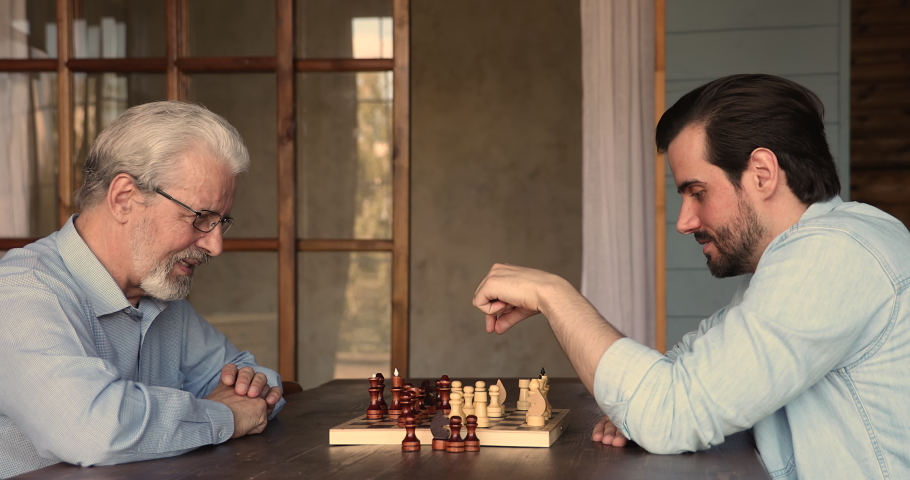 Happy 60s old mature man enjoying playing chess with grown son, making strategic moves, planning steps on chessboard, having fun entertaining together at home, hobby pastime activity concept. Royalty-Free Stock Footage #1067337367