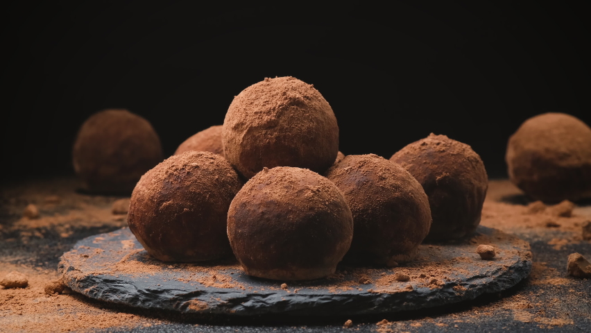 Chocolate pouring on truffles, melted chocolate candy icing on black slate with cocoa powder, 4k ProRes uncompressed Royalty-Free Stock Footage #1067340943