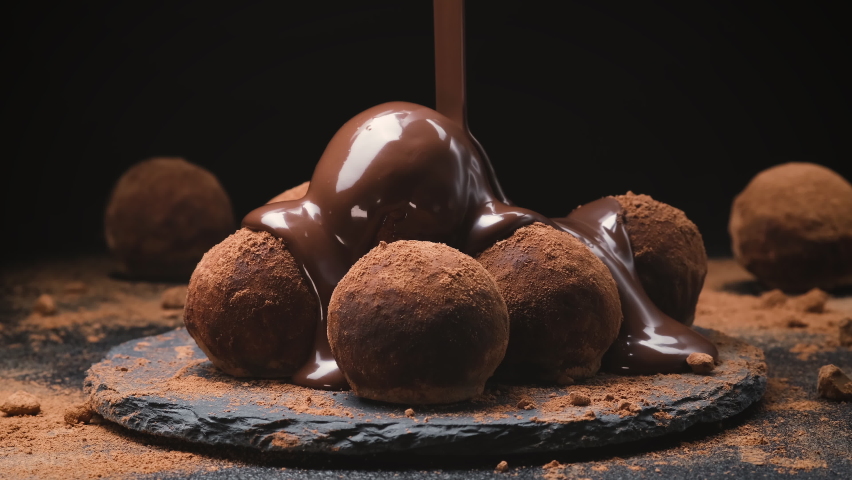 Chocolate pouring on truffles, melted chocolate candy icing on black slate with cocoa powder, 4k ProRes uncompressed | Shutterstock HD Video #1067340943