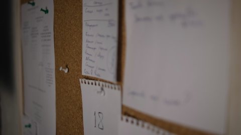 Note paper on a cork board. Notes, stickers, reminders. Selective focus. Men's hands are moving. Select a reminder