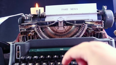 old typewriter on table, words fake news are printed on paper in large size, candle is burning, retro style, concept of information hoax in social media, misleading, exposing deception	
