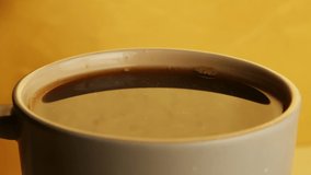 Slow motion video clip of cream being poured into a full cup of coffee, splashing and creating a delicious mess