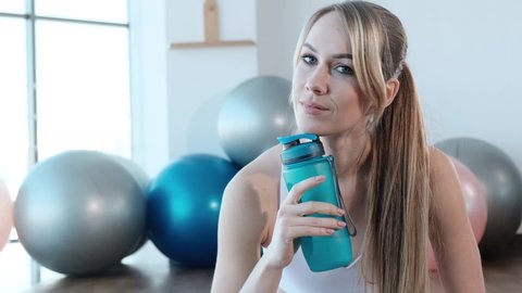 A young woman is resting after a hard workout in the gym and holding a bottle of water in her hands