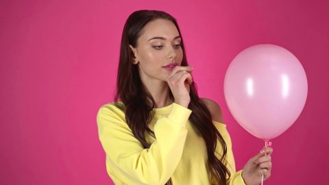 slow motion shoot of young woman piercing with needle pink air balloon and showing surprised emotion