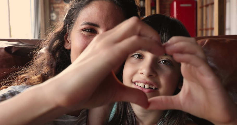 Happy beautiful mother and little 10s adorable daughter faces seen through joined fingers making heart shape, close up. Symbol of love and cherish of mom and kid, donation, sincere feelings concept | Shutterstock HD Video #1067349562