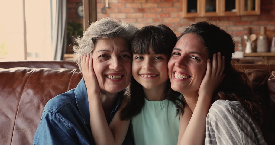 Grandma, mom and daughter of sit on sofa at home smile look at camera. Cute girl touch cheeks of mom and elderly granny enjoy moment of tenderness. Three generations of women family portrait concept Royalty-Free Stock Footage #1067349733