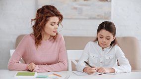 mother talking to daughter while she writing in copy book and showing yes gesture at desk