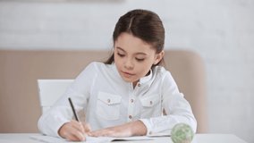 smiling cute preteen schoolgirl doing homework and writing in copy book at desk